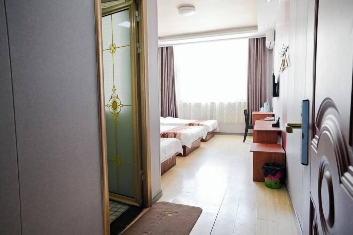 A hotel room with a bed, a desk, a chair, a small table, a trash bin, and a door.