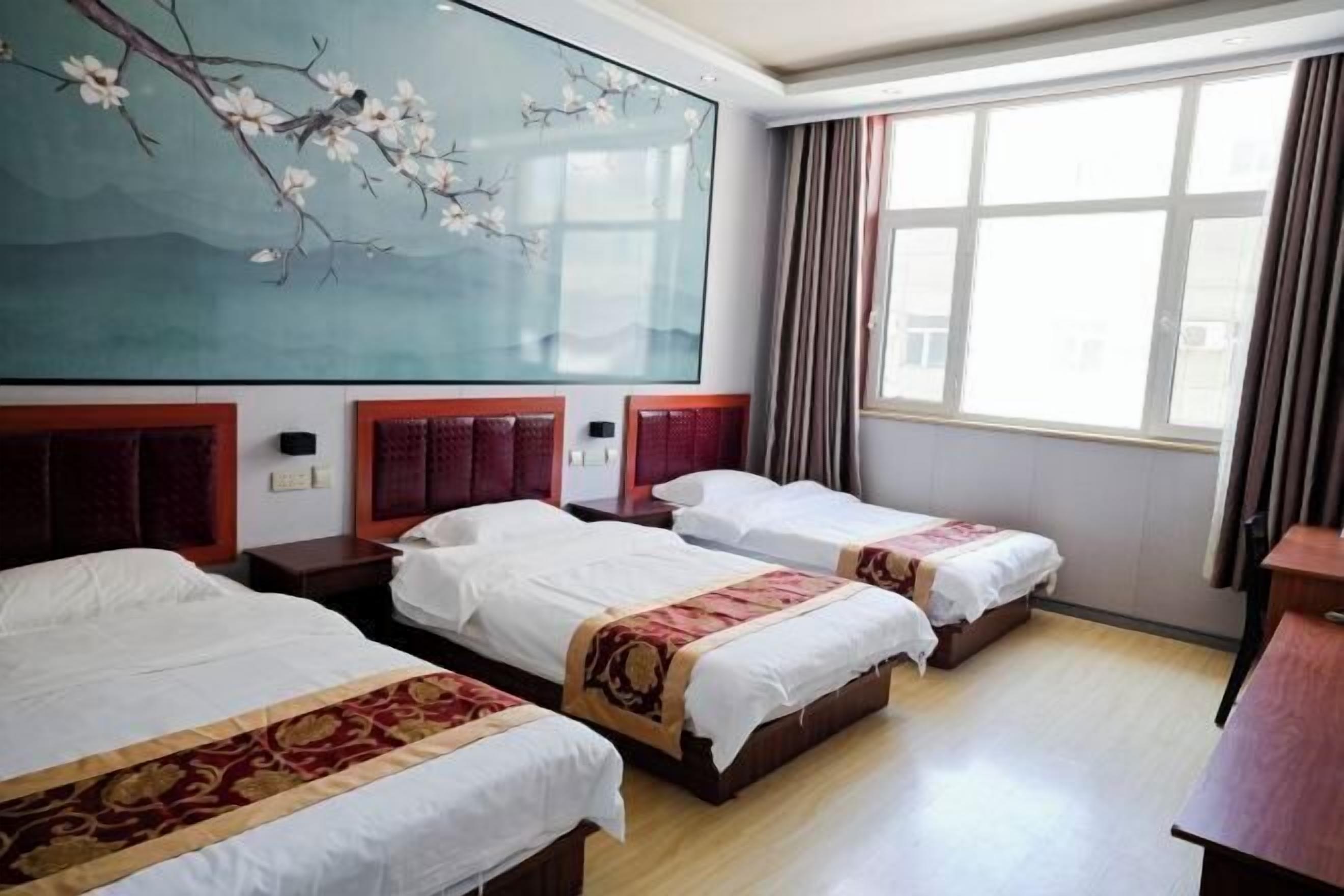 A hotel room with three beds, a large window, and a wall painting.