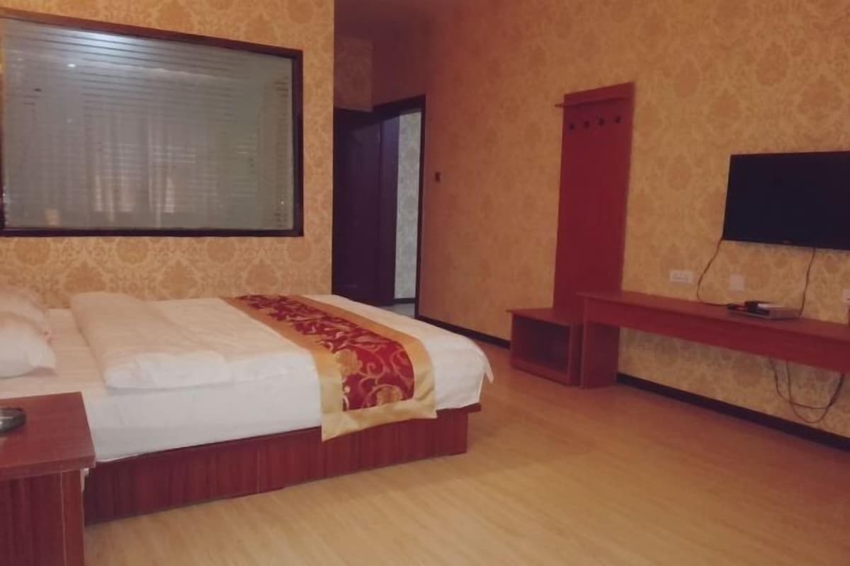 A hotel room with a large bed, a television, a wooden bench, and a wardrobe.