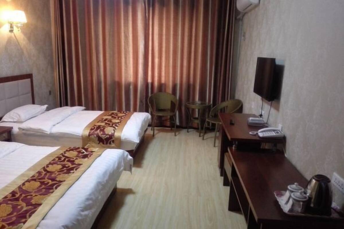 A hotel room with two beds, a desk, a chair, a telephone, and a television.
