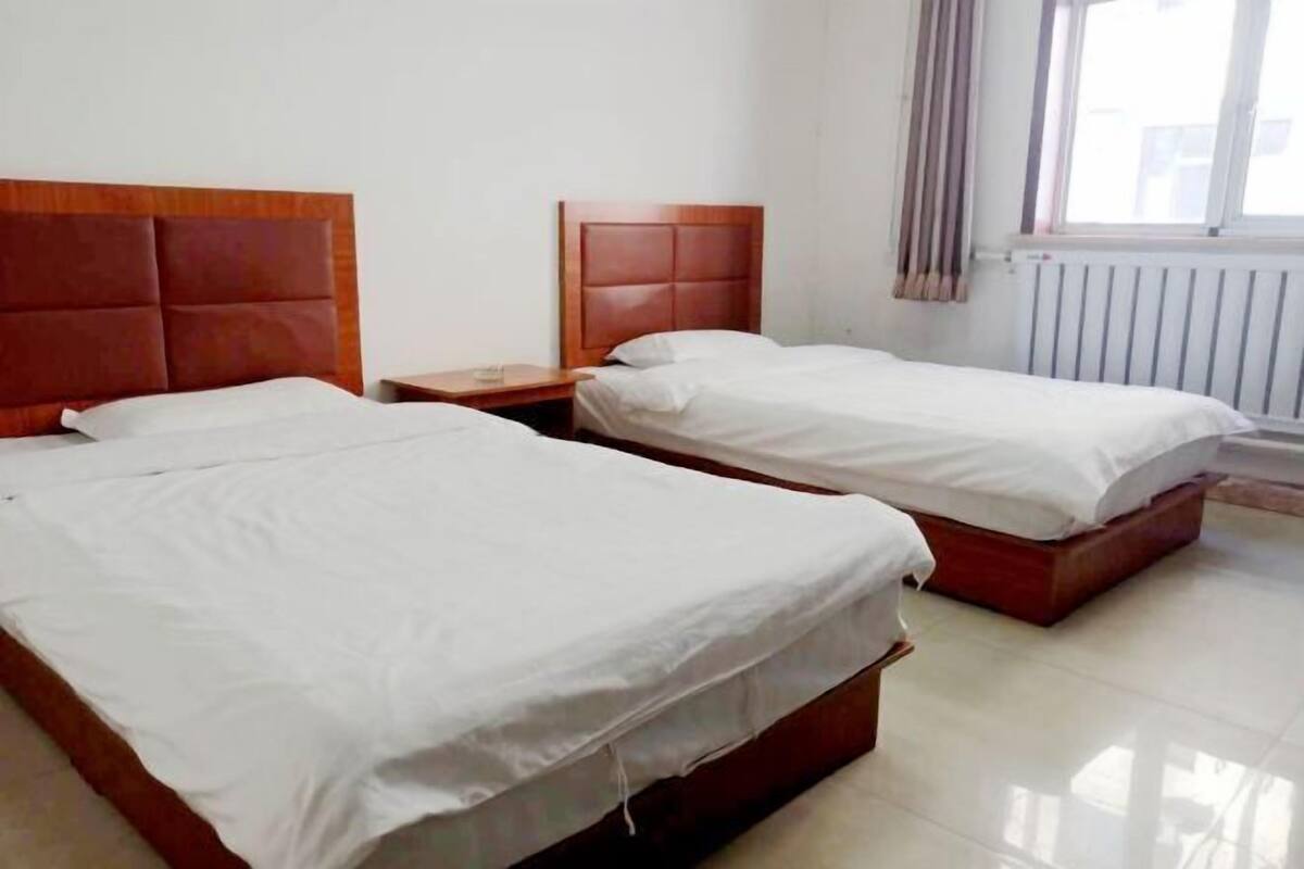 A room with two beds, a nightstand, and a window with curtains.