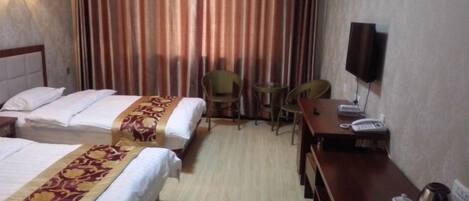 A hotel room with two beds, a desk with a telephone, a chair, and a TV on the wall.