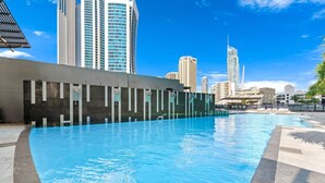 A swimming pool with a modern design, surrounded by tall buildings and a clear blue sky.