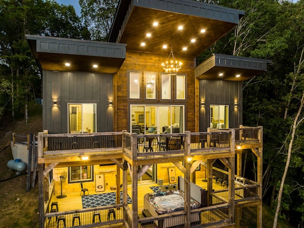 A two-story wooden cabin with a balcony, a hot tub, and a dining area.