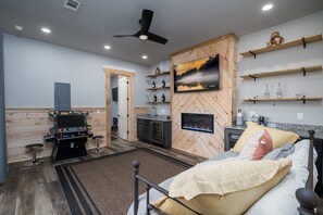 A compact room with a bed, a kitchenette, a mounted TV, and a ceiling fan.