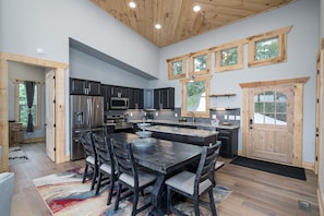 A modern kitchen with dark cabinetry, a large island, and a dining area with chairs.