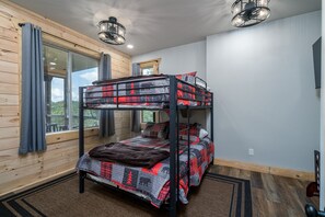 A bunk bed room with a large window, wooden walls, and a ceiling light fixture.