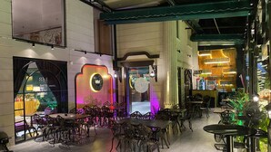 An indoor dining area with ornate metal chairs and tables, a neon sign, and a view of the street outside. - Sabina Boutique Hotel 3 (Ho Chi Minh City)