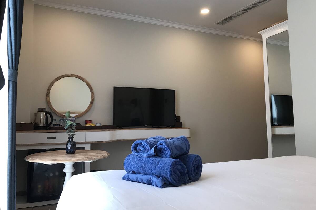 Ein Hotelzimmer mit einem Bett, einem Fernseher, einem kleinen Tisch mit einer Vase und einem Spiegel an der Wand.
