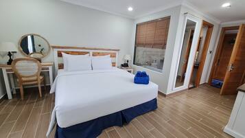 Habitación de hotel con una cama grande, un escritorio con silla, un espejo y una ventana con persianas.