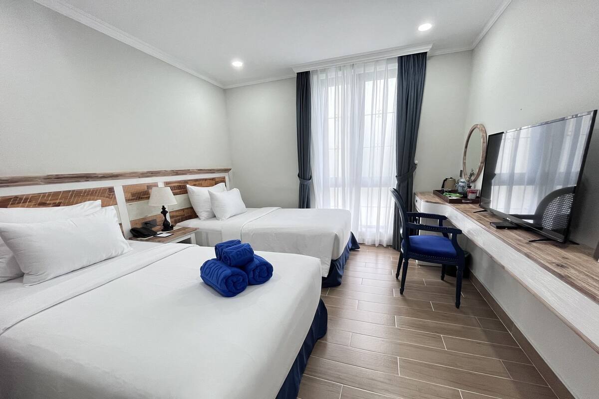Ein Hotelzimmer mit zwei Betten, einem Schreibtisch mit Stuhl, einem Fernseher und einem Fenster mit Vorhängen.