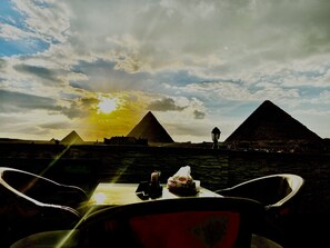 A table with chairs facing a view of the pyramids under a cloudy sky.