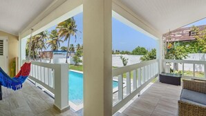 A covered outdoor area with a pool, a hammock, and wicker furniture. - Coco Chalet | Villa with private pool and steps from Playa Peñón Brusi (Camuy)