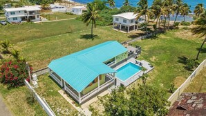 A two-story house with a swimming pool, surrounded by a grassy lawn and palm trees, with a view of the ocean. - Coco Chalet | Villa with private pool and steps from Playa Peñón Brusi (Camuy)