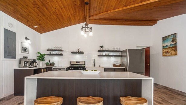 A modern kitchen with a large island, wooden stools, and a wooden ceiling. - Coco Chalet | Villa with private pool and steps from Playa Peñón Brusi (Camuy)