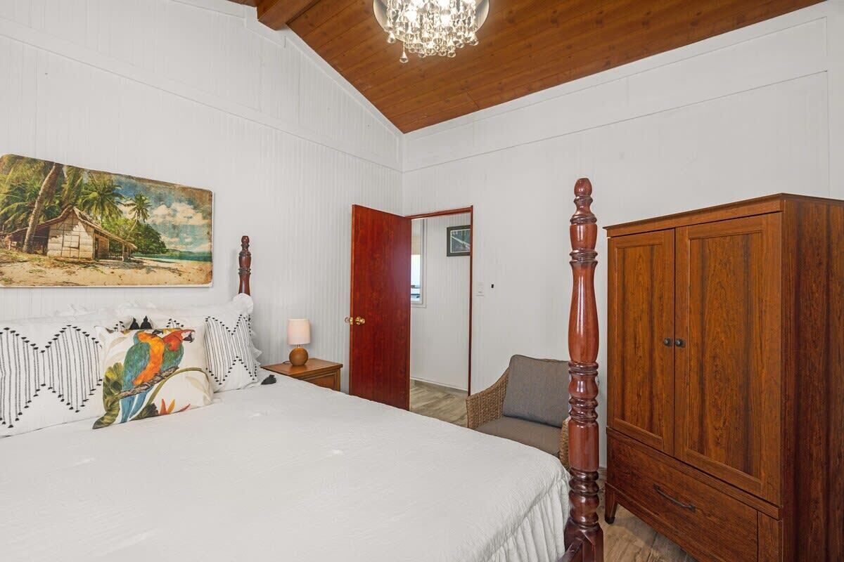 A bedroom with a bed, a wooden wardrobe, a nightstand, a lamp, a chair, and a door.