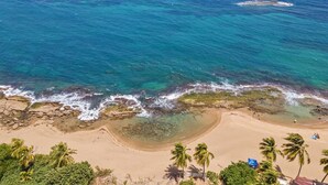 A beach with clear turquoise water, rocky shoreline, and palm trees. - Coco Chalet | Villa with private pool and steps from Playa Peñón Brusi (Camuy)