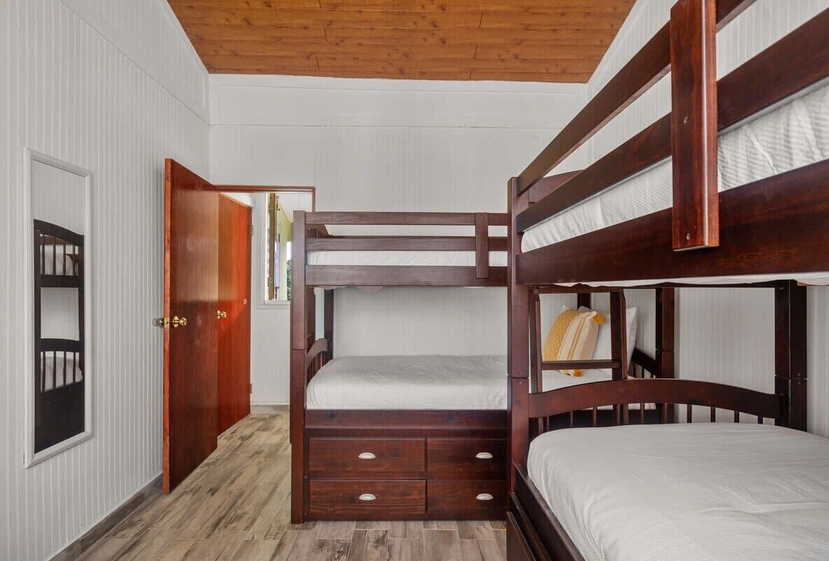 A bunk bed room with a wooden ceiling, white walls, and a wooden floor.