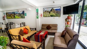 Un hall d’hôtel avec un ensemble de canapés, une table basse et un téléviseur. Des tableaux ornent les murs et une plante en pot est posée dans un coin.