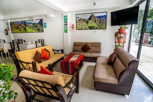 Un hall de hotel con un conjunto de sofás, una mesa de centro y una televisión. Hay cuadros en la pared y una planta en maceta.