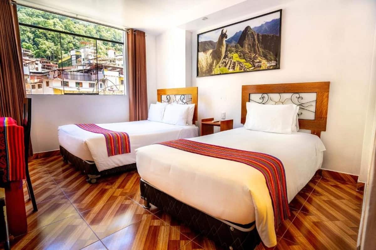 Een hotelkamer met twee bedden, houten vloeren, een raam met uitzicht op een stadsbeeld en een schilderij aan de wand.