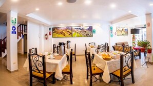 Un coin repas avec des tables préparées pour le petit-déjeuner, un grand tableau accroché au mur et un escalier menant à un autre étage.