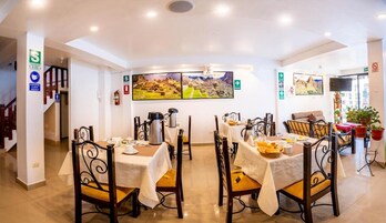 Un comedor con mesas dispuestas para el desayuno, un cuadro grande en la pared y una escalera que sube a otro nivel.