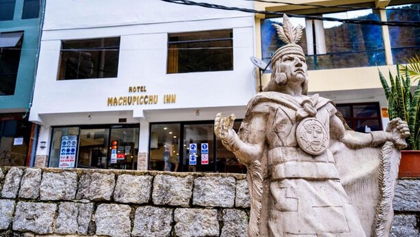 Une statue de pierre se trouve devant un hôtel appelé « Hotel Machupicchu Inn ».