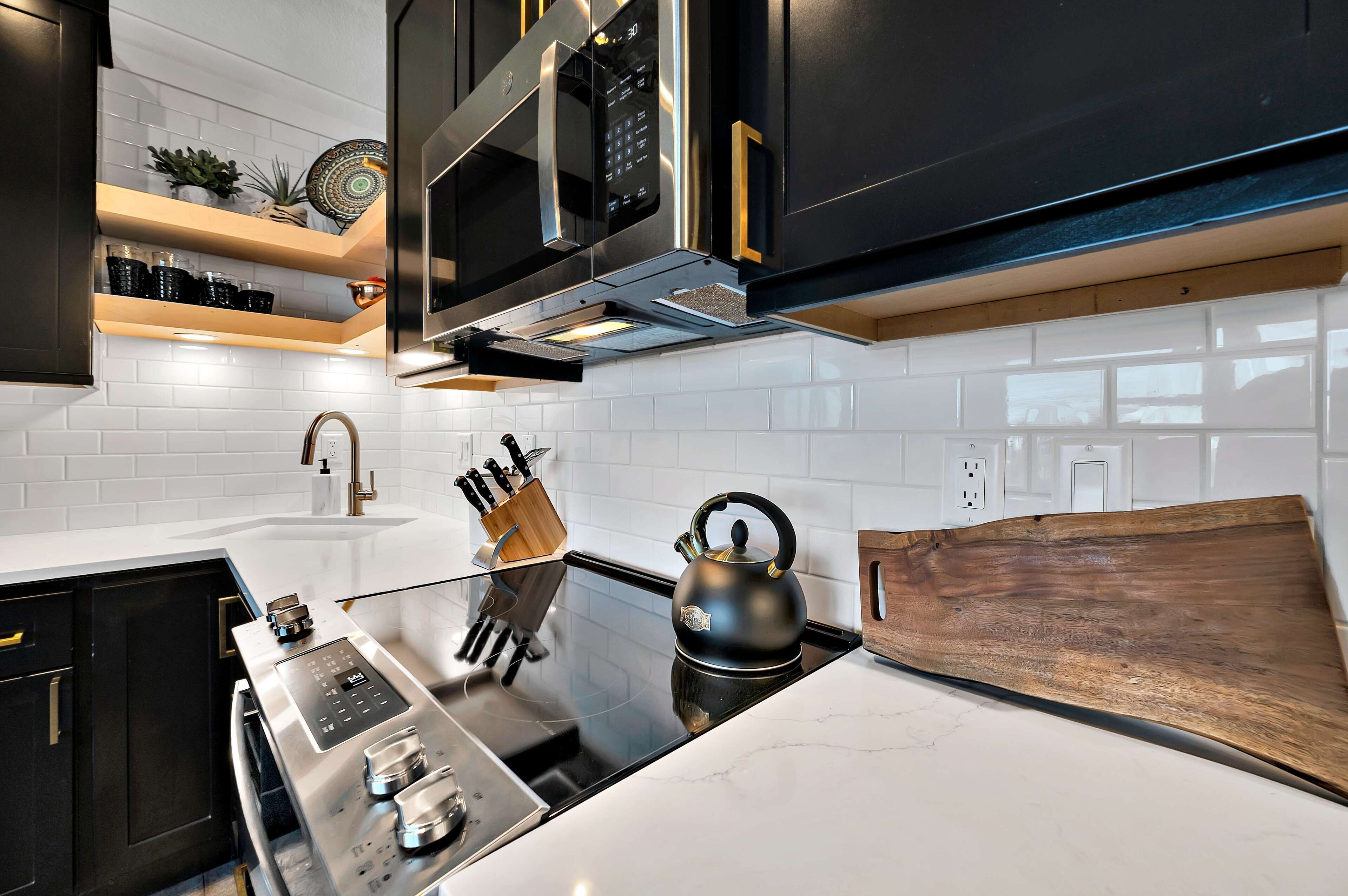 A modern kitchen with a black kettle, stainless steel appliances, and wooden shelves.