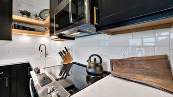 A modern kitchen with a black kettle, stainless steel appliances, and wooden shelves.
