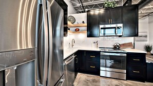 Une cuisine moderne dotée d’appareils électroménagers en acier inoxydable, de meubles de rangement noirs et d’un plan de travail en marbre.