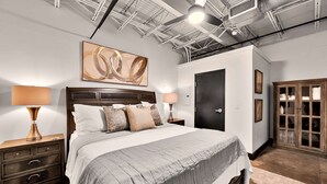 Une chambre avec un grand lit, deux tables de chevet avec des lampes, une armoire et un plafond avec des poutres apparentes.