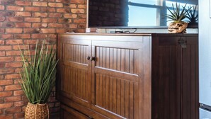 Une pièce avec un mur en briques, un meuble en bois doté de tiroirs, un grand téléviseur à écran plat et une plante en pot.