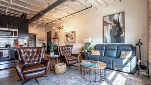 Un salon moderne avec des fauteuils en cuir, un canapé bleu, une table basse et un grand tableau abstrait accroché au mur.