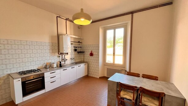A compact kitchen with a gas stove, oven, and white cabinetry. There is a dining area with a table and chairs, and a window providing natural light. - In the center of Porretta Terme (Porretta Terme)