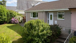 A single-story house with a grey exterior and a brown roof. It features a front door, two windows, and a small porch area. - Ballyroan - Peaceful Dog Friendly Cottage (Tenby)