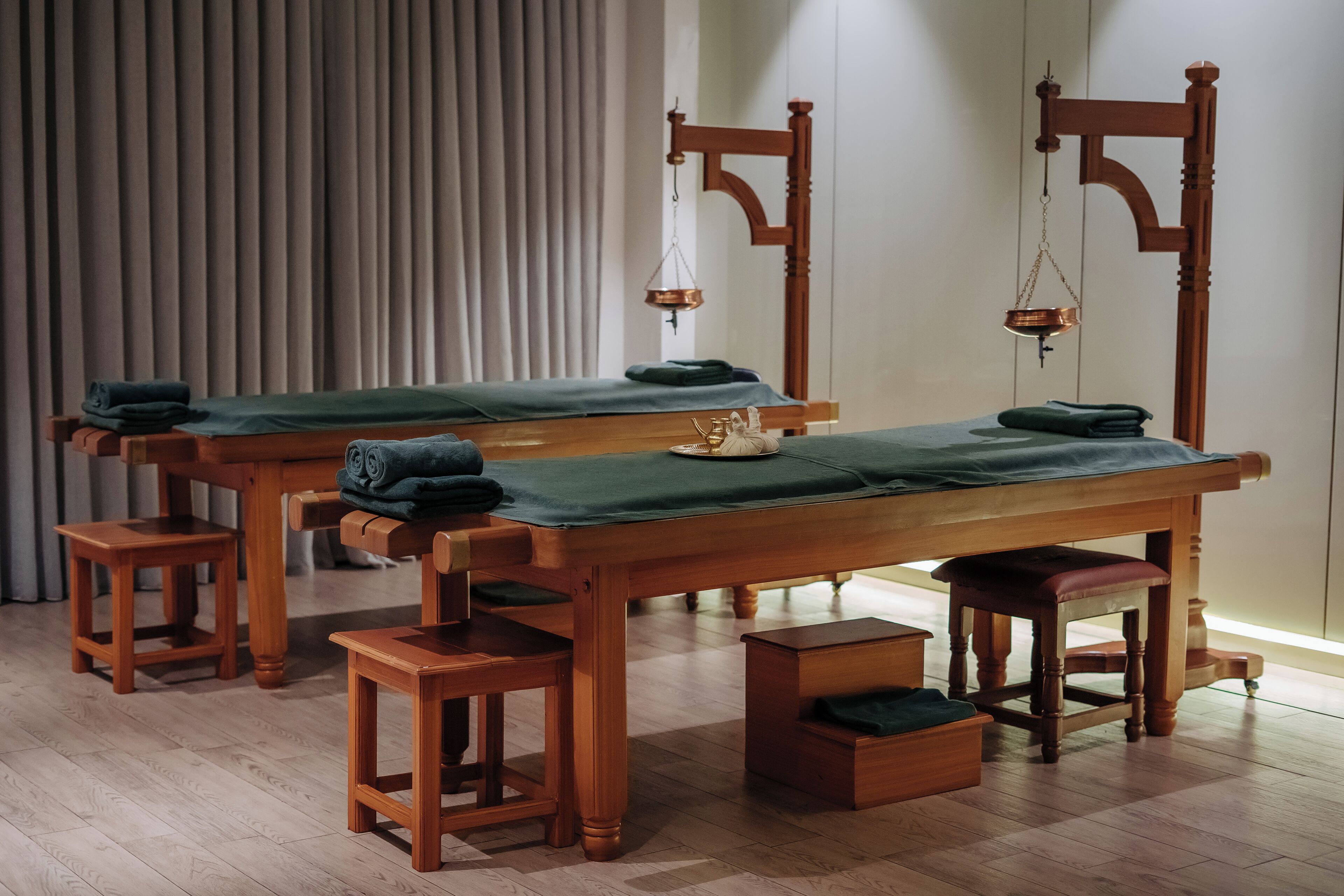Un cuarto de masajes tradicional con mesas y bancos de madera, una balanza y una colchoneta verde.