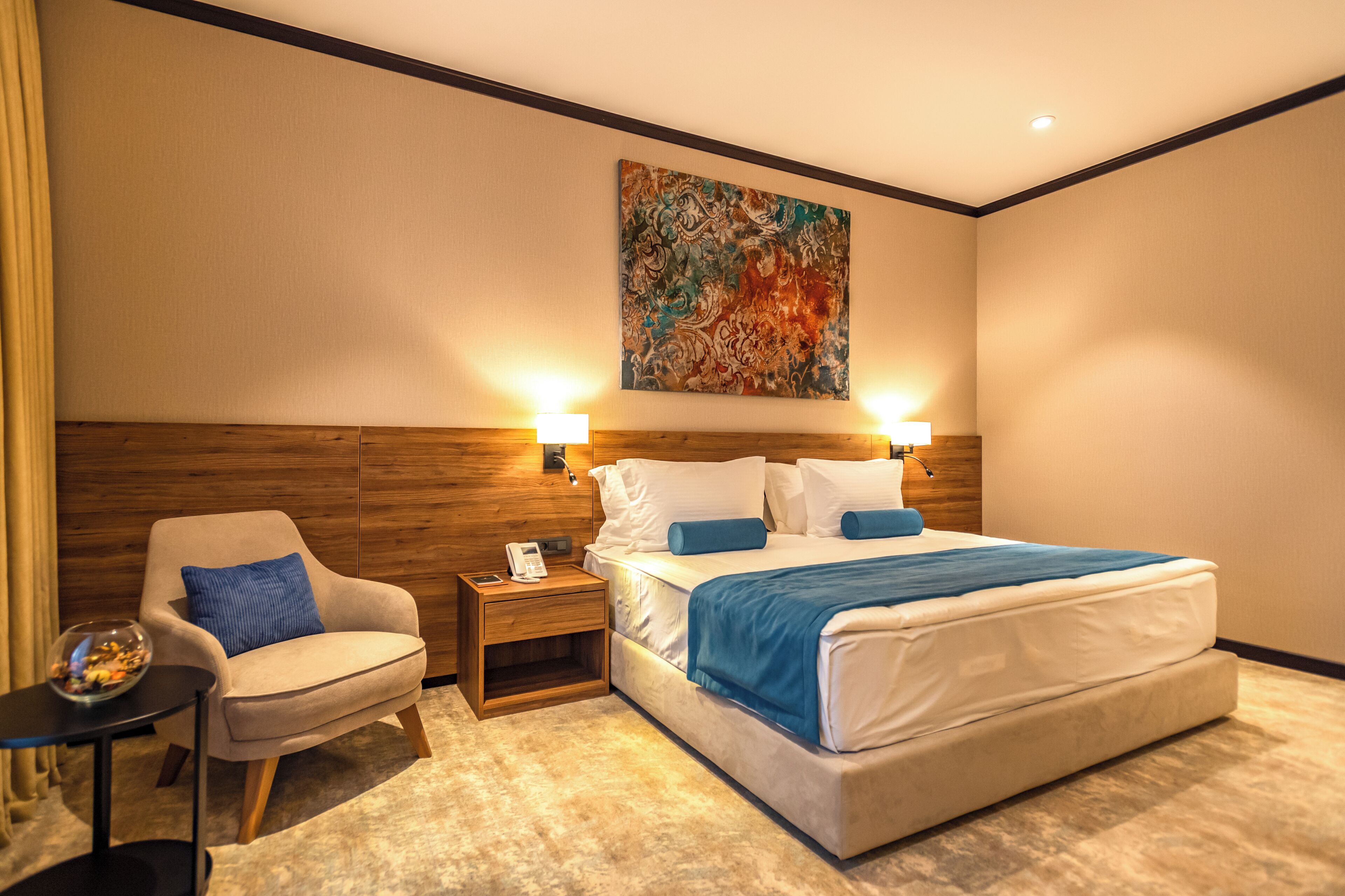 A hotel room with a bed, a chair, a nightstand, and a painting on the wall.