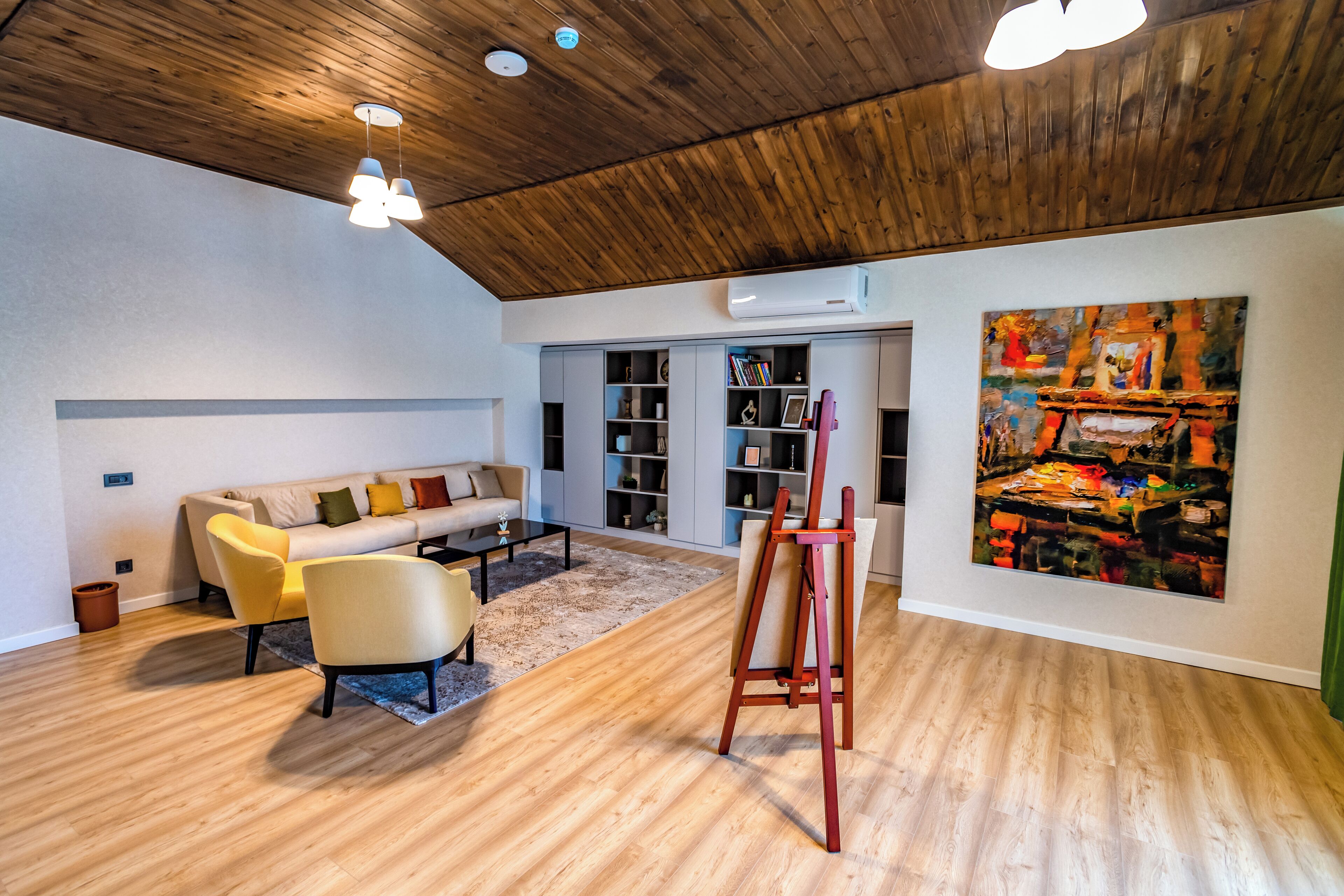 Un salon avec un plafond en bois, un canapé, une table basse, un tableau et des étagères intégrées.