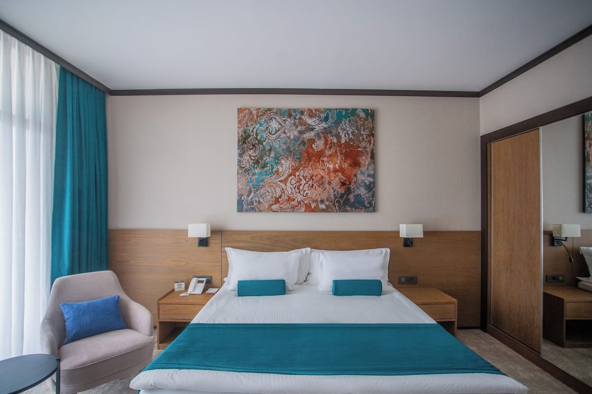 Ett hotellrum med en stor säng, två sängbord, en stol och en stor, abstrakt målning på väggen.