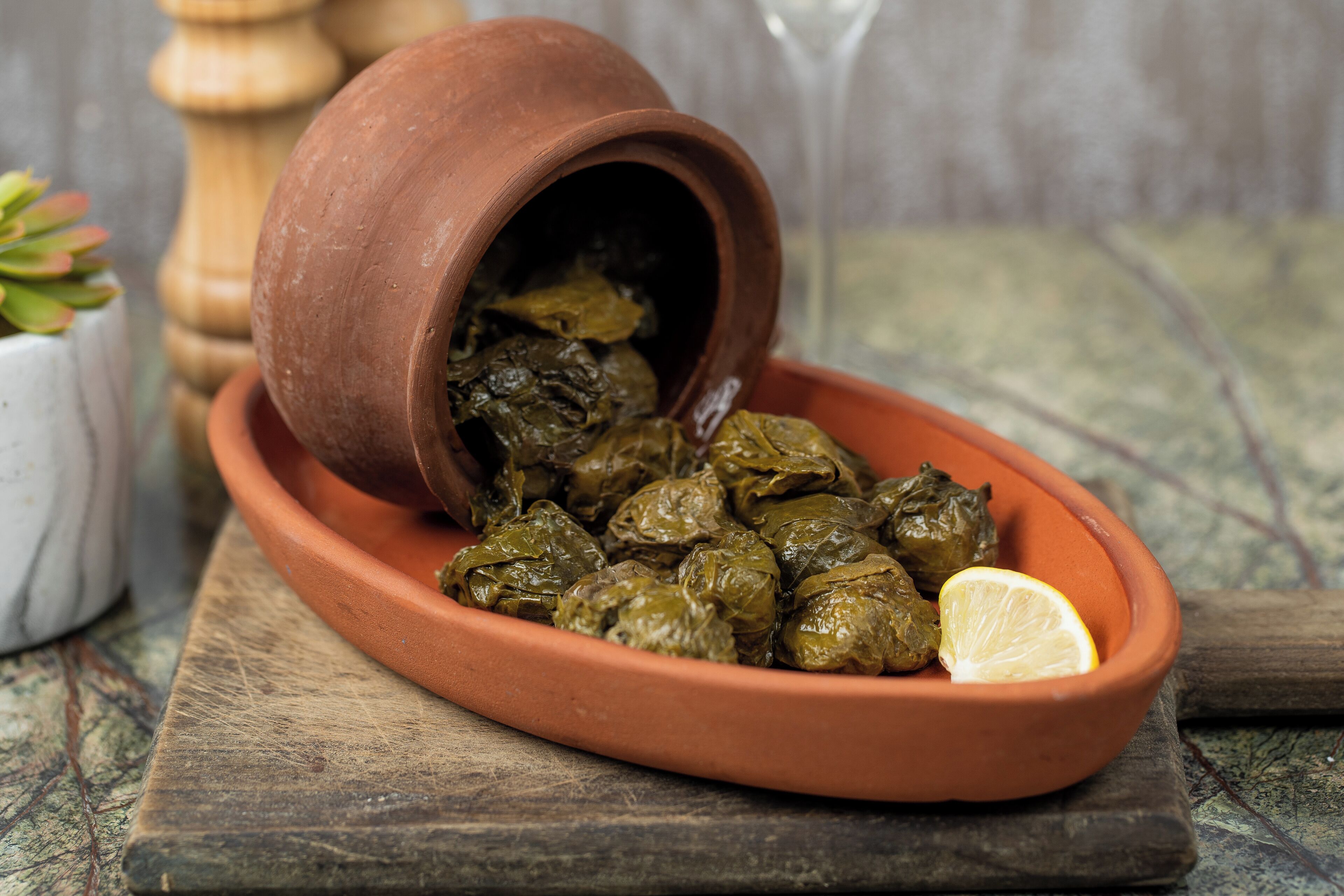 A terracotta dish with stuffed grape leaves and a lemon wedge on a rustic wooden table.