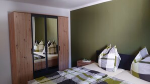 A bedroom with a wooden wardrobe, a bed with a striped quilt, and a nightstand with a lamp.