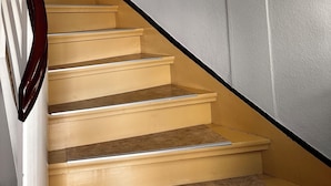 A staircase with wooden steps and a dark handrail, leading to a landing with a white wall.