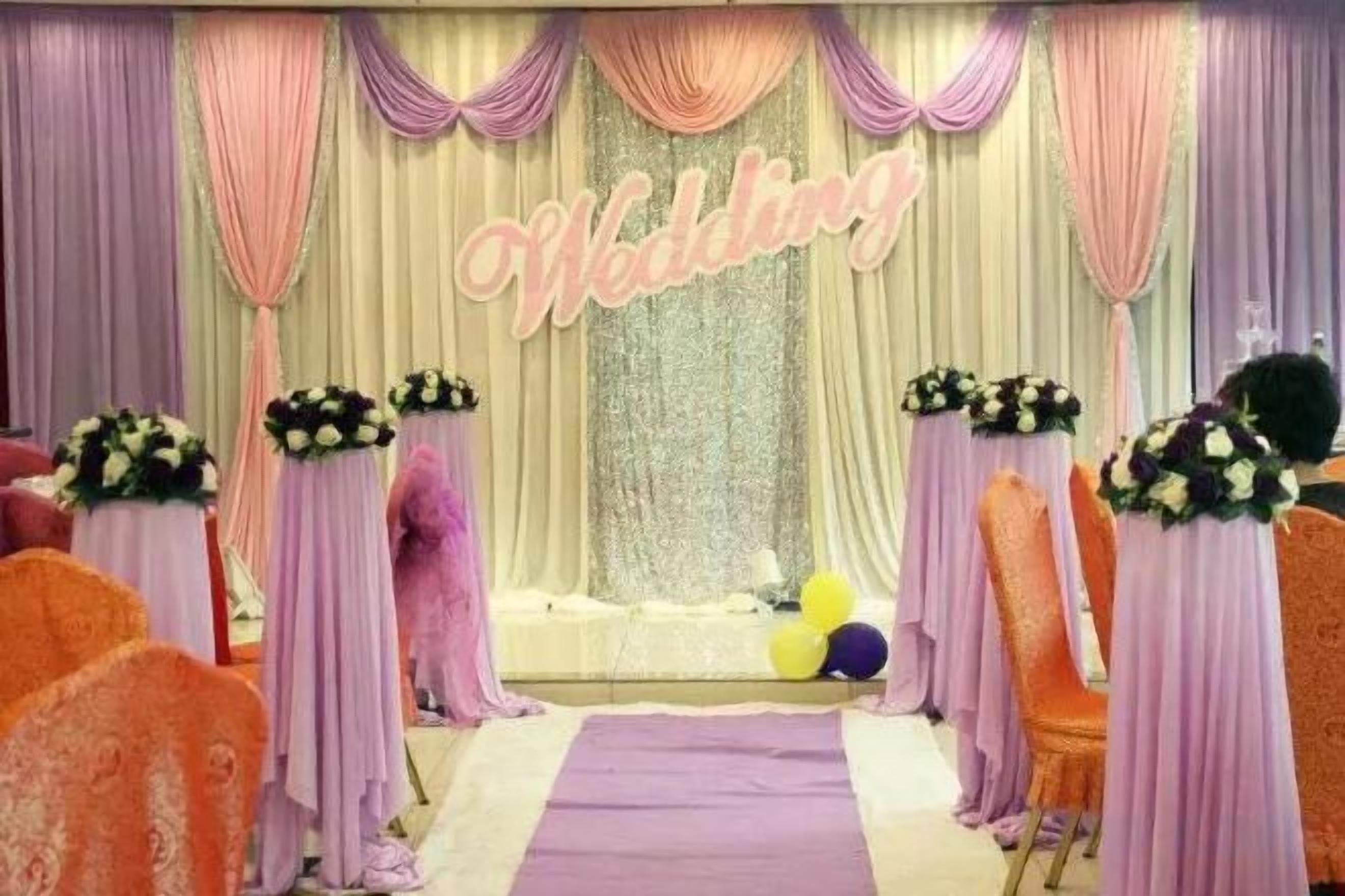 A wedding stage with a 'Wedding' sign, floral centerpieces, and a purple aisle.