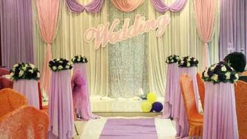 A wedding stage with a 'Wedding' sign, floral centerpieces, and a purple aisle.