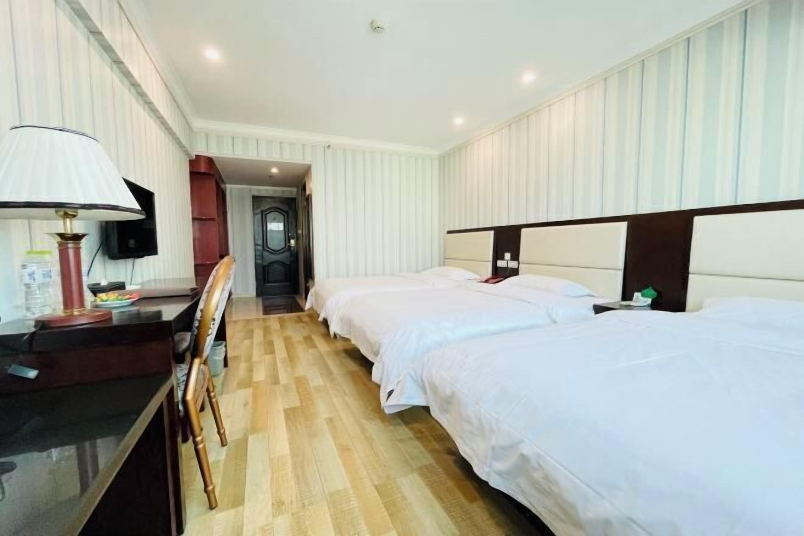 A hotel room with two beds, a desk with a lamp, and a television.