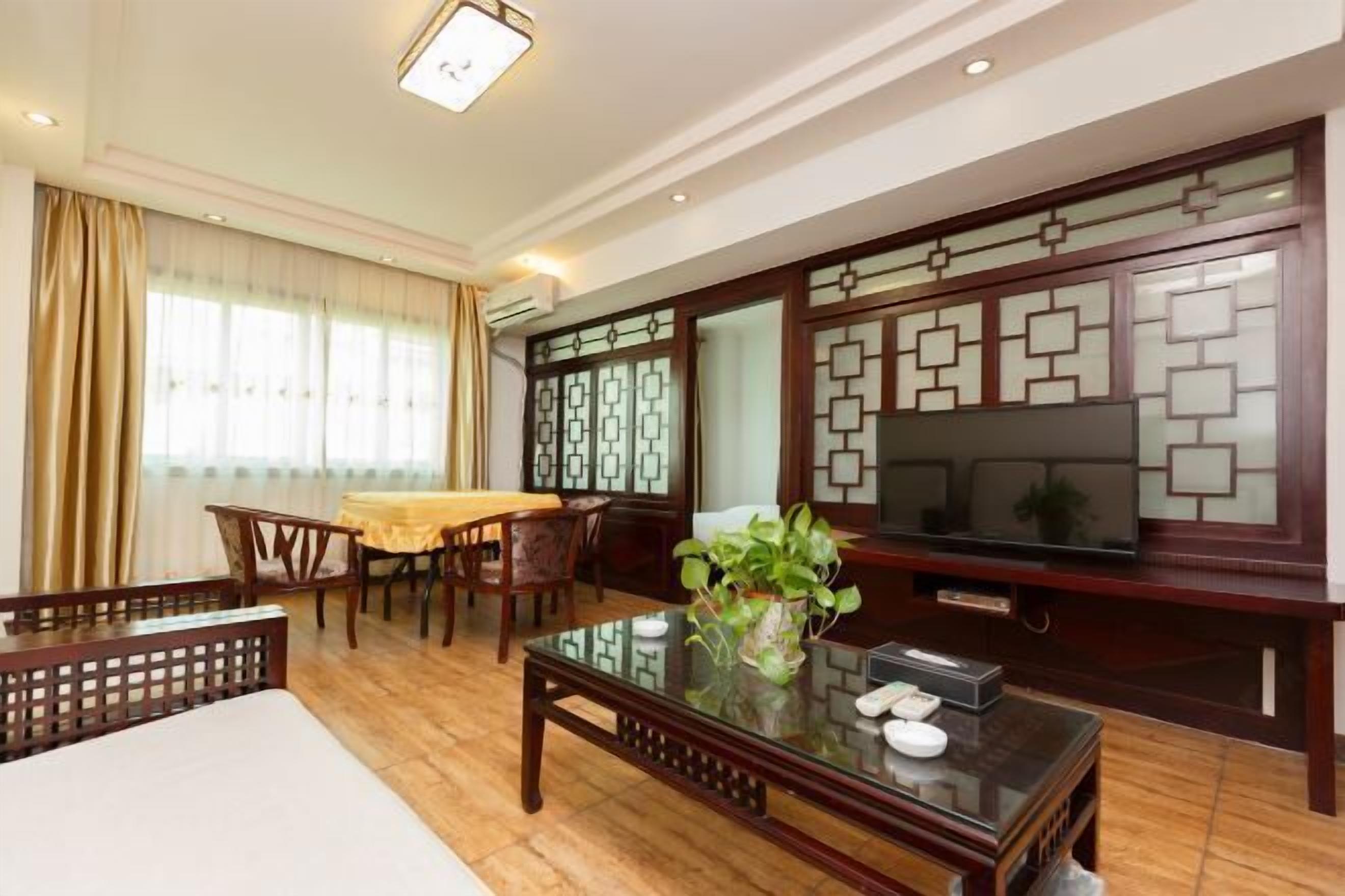 Un salón comedor de estilo tradicional con un mueble de televisión de madera, una mesa de centro de vidrio y una zona de comedor con mantel amarillo.