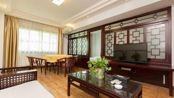 Un salón comedor de estilo tradicional con un mueble de televisión de madera, una mesa de centro de vidrio y una zona de comedor con mantel amarillo.
