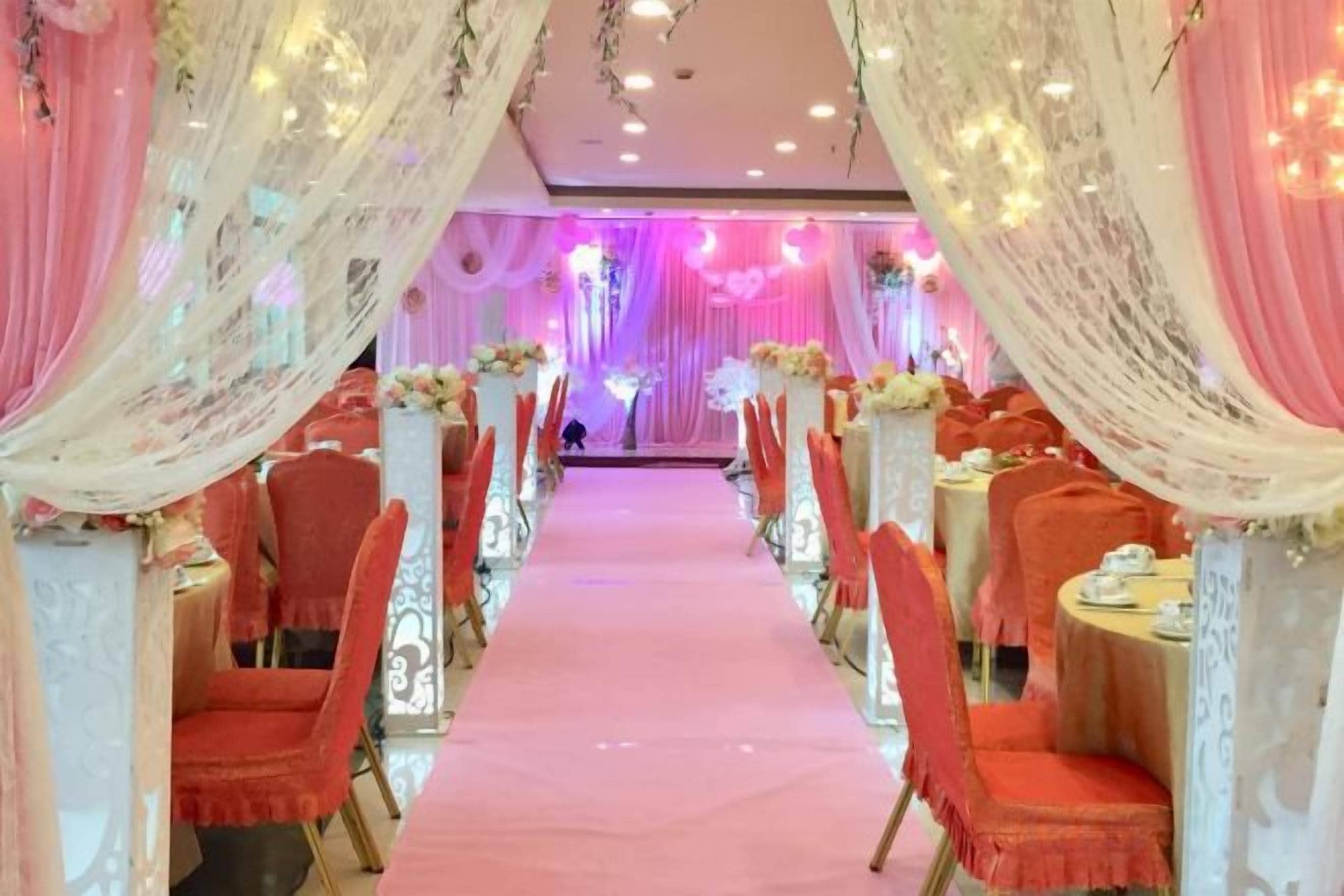 A banquet hall with rows of tables and chairs, a central aisle, and draped curtains.