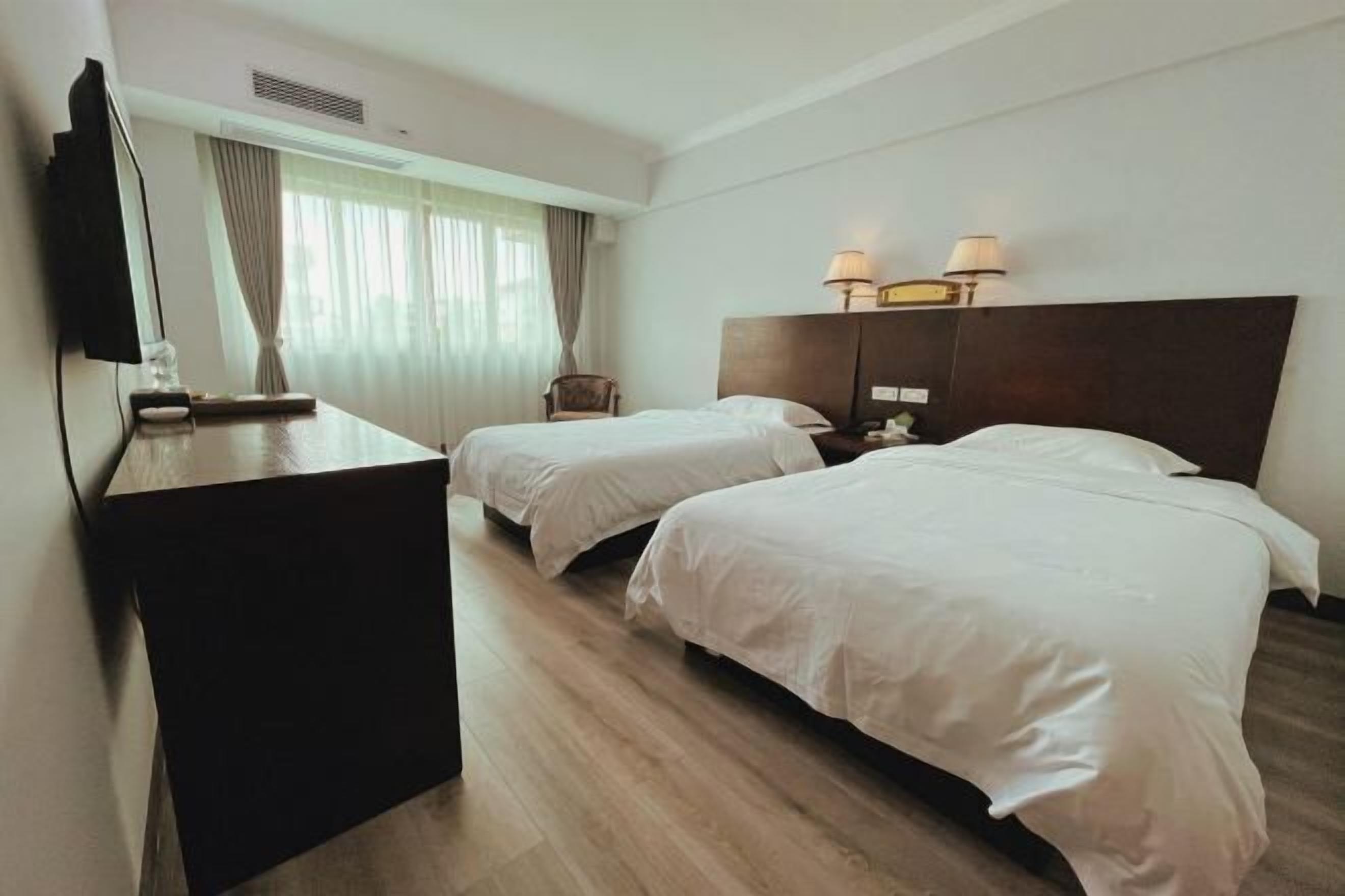 Una camera d'albergo con due letti, una scrivania, una televisione e una finestra con tende.